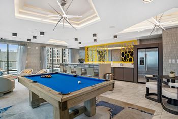 A pool table in a living room with a bar and a kitchen